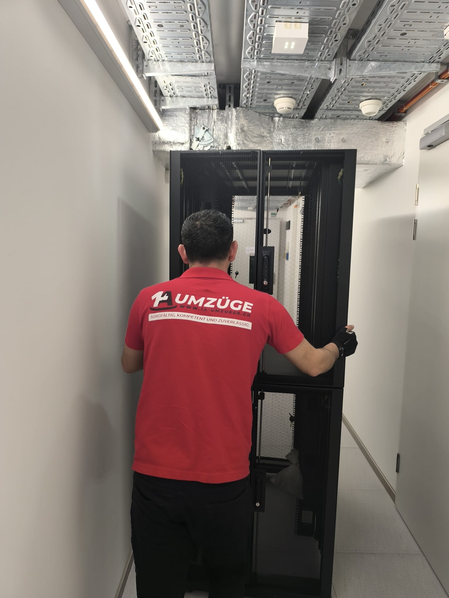 Ein Mitarbeiter positioniert einen Serverschrank in einem schmalen Durchgang