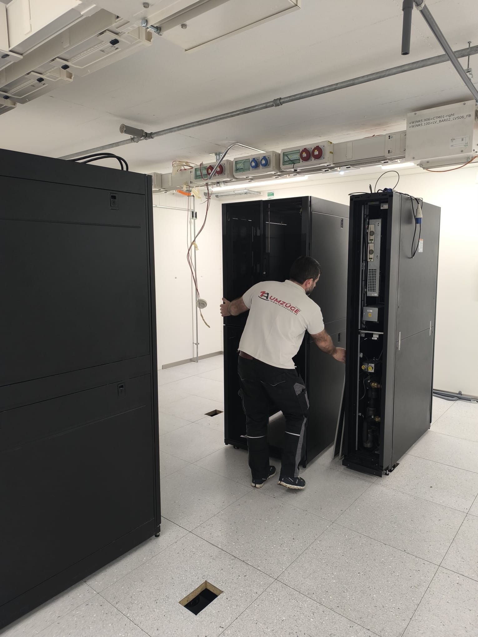 Ein Mitarbeiter an einem geöffneten Serverschrank neben weiteren Schränken im Rechenzentrum