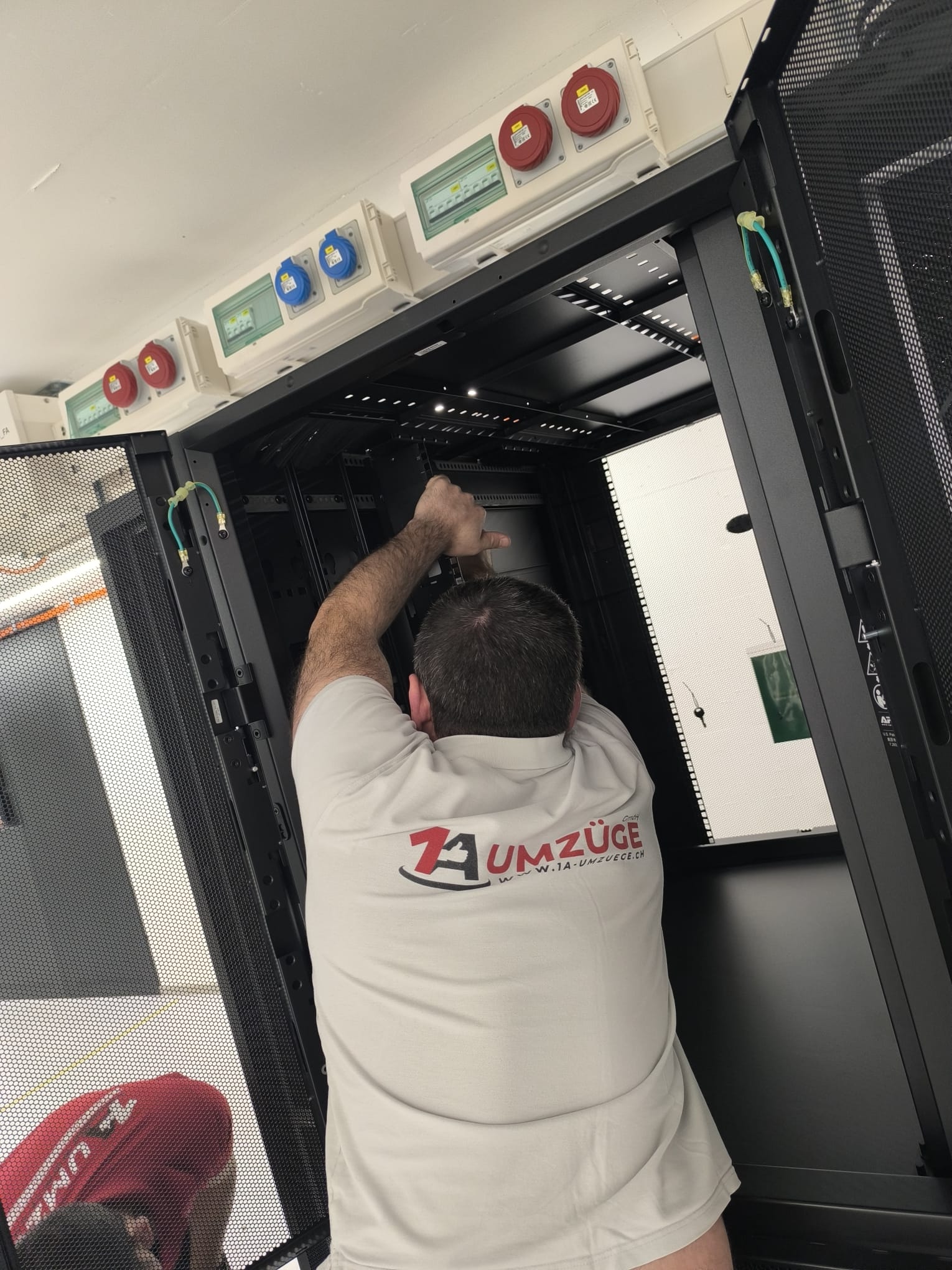 Ein Mitarbeiter arbeitet im oberen Innenbereich eines geöffneten Serverschranks